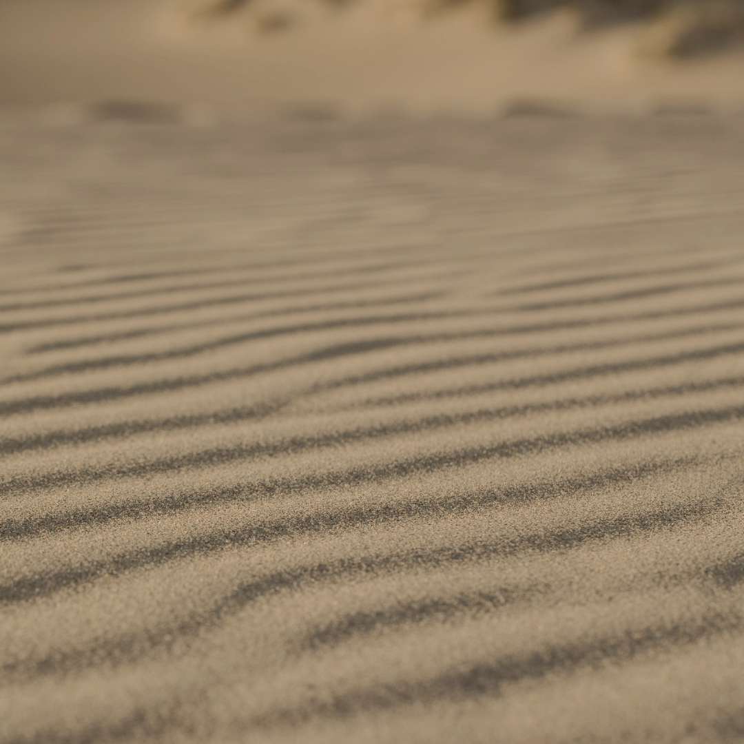 Estetyczne, minimalistyczne zdjęcie przedstawiające piasek ułożony w regularne fale. Wizualna metafora naturalnego 'Flow' i kobiecej produktywności, która przeciwstawia się sztywnym systemom typu "5:00 rano".