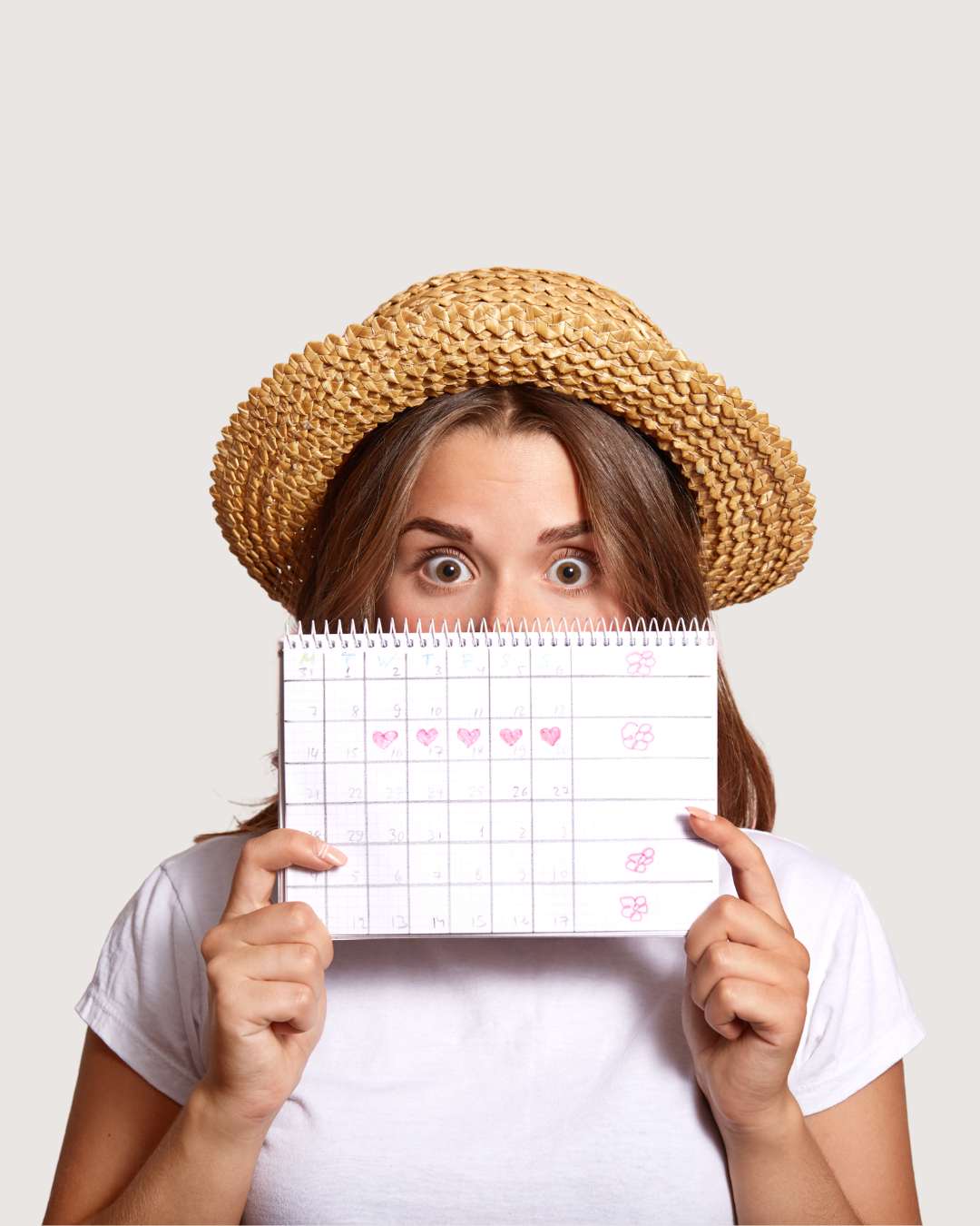 Estetyczne zdjęcie kobiety w słomkowym kapeluszu, która trzyma przed twarzą różowy kalendarzyk cyklu menstruacyjnego. Wizualizacja strategicznego planowania zadań w biznesie solo zgodnie z modelem FlowSync.